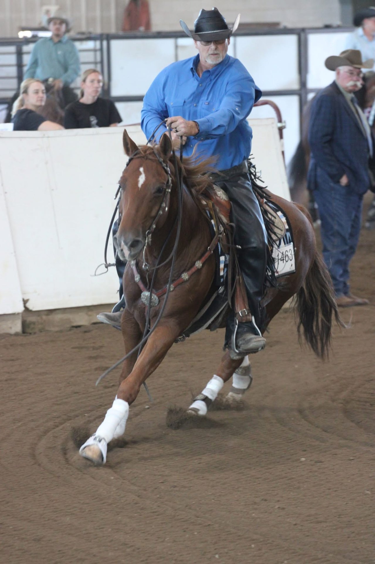 Reining rider in a blue shirt performing a sliding stop in an indoor arena